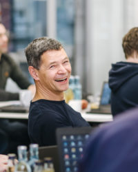 Gruppe sitzt am Tisch. Mann lacht.